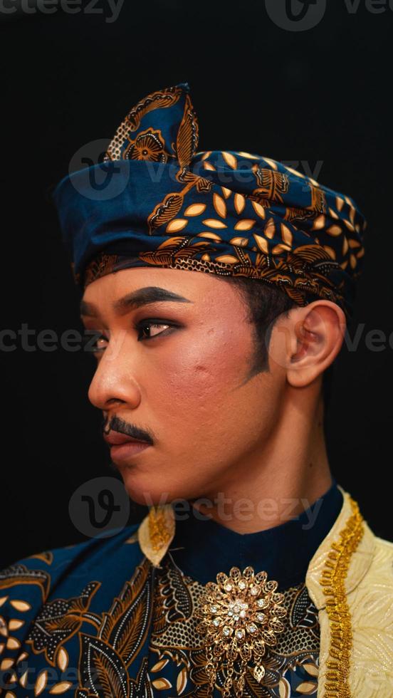 ett asiatisk man bär en traditionell kostym med skön motiv på hans skjorta och bär en bandana kallad en bendo i en rum foto