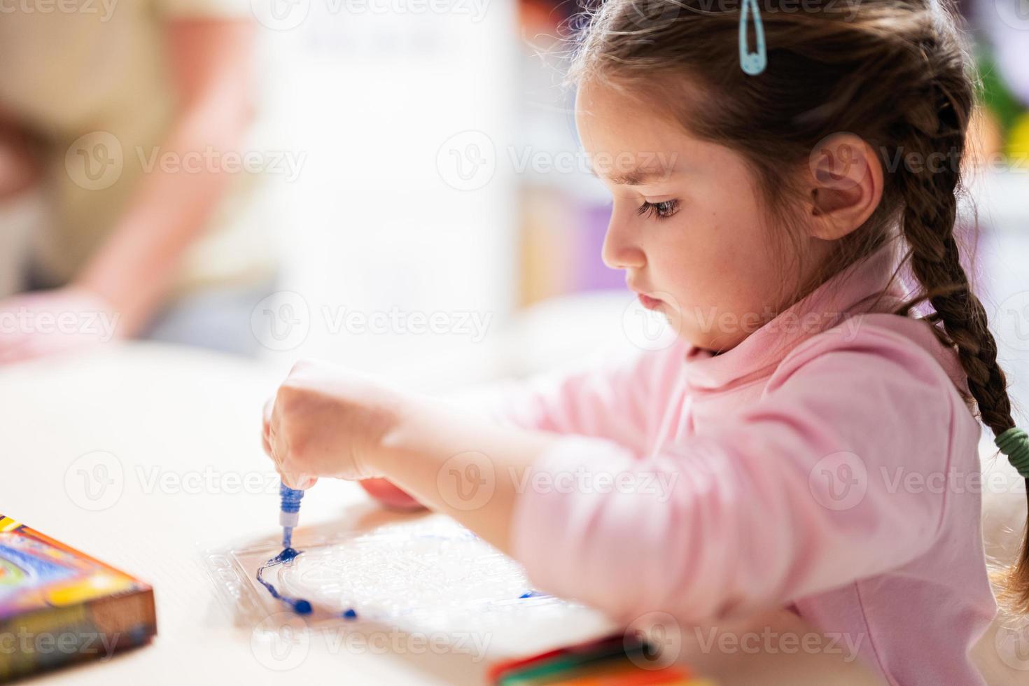 liten flicka med pigtails dekorera konst med glitter dekor rör av måla. foto