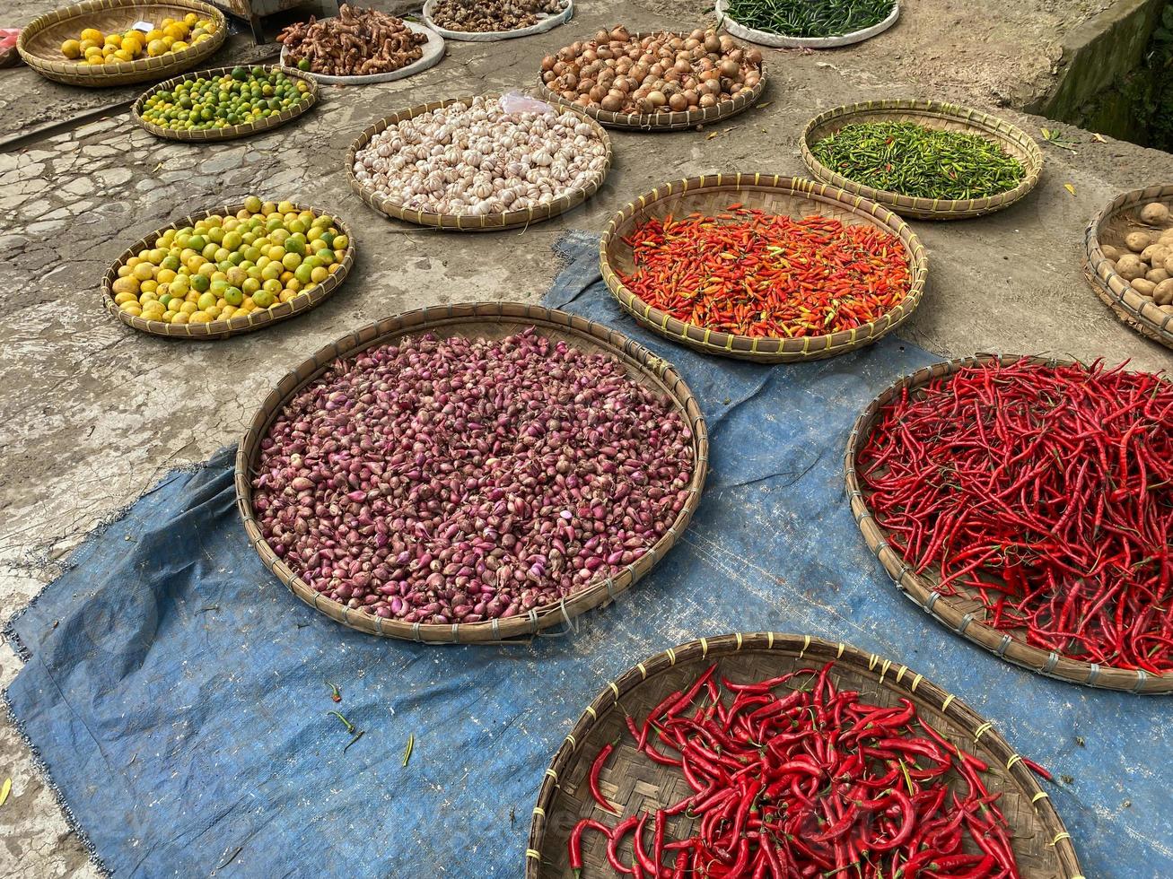 olika grönsaker tomater, chili, röd lök, majs, morot, kalk, vitlök varelse såld på asiatisk traditionell marknadsföra. färgrik grönsaker på runda bambu bricka på traditionell marknadsföra golv foto