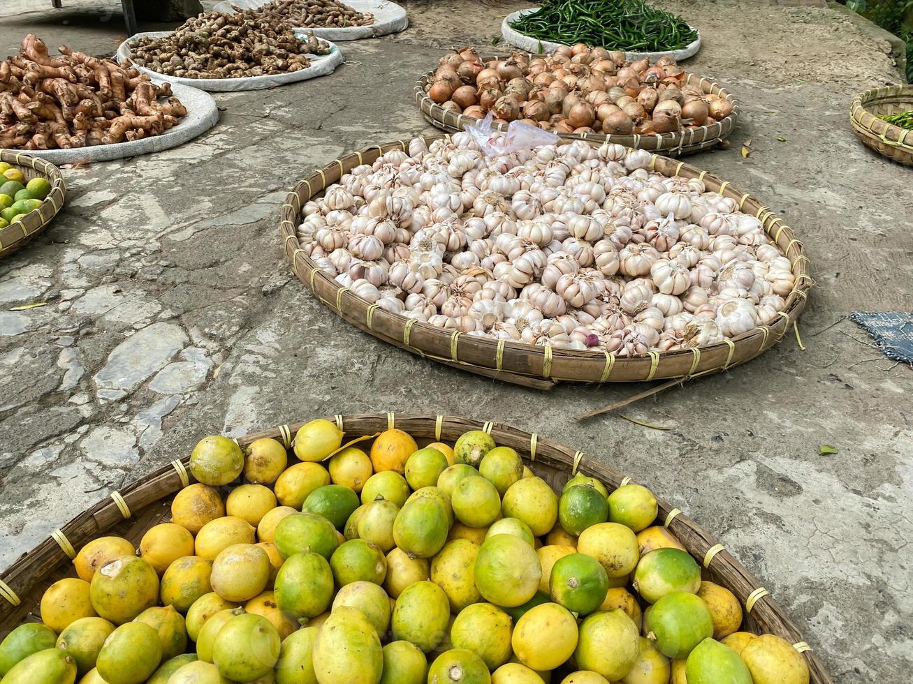 olika grönsaker tomater, chili, röd lök, majs, morot, kalk, vitlök varelse såld på asiatisk traditionell marknadsföra. färgrik grönsaker på runda bambu bricka på traditionell marknadsföra golv foto