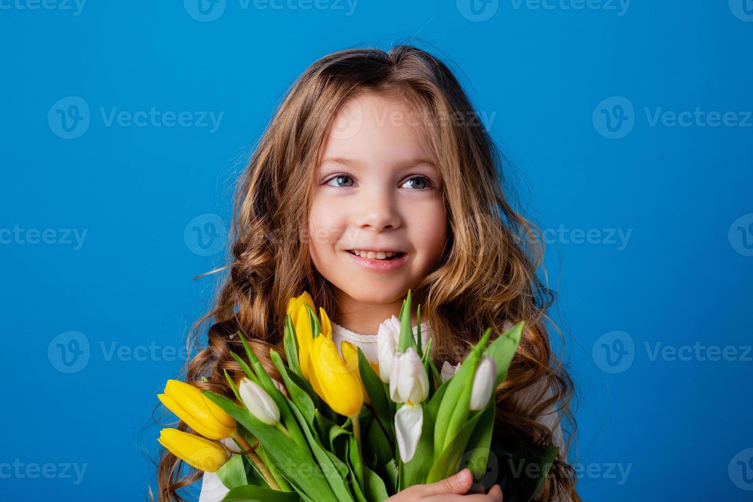 porträtt av en charmig leende liten flicka med en bukett av tulpaner i henne händer. livsstil. färsk blommor. internationell kvinnors dag. Plats för text. hög kvalitet Foto