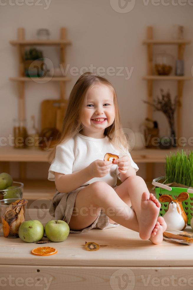 söt liten flicka äter naturlig pastill på Hem i en trä- kök. mat för barn från naturlig Produkter foto