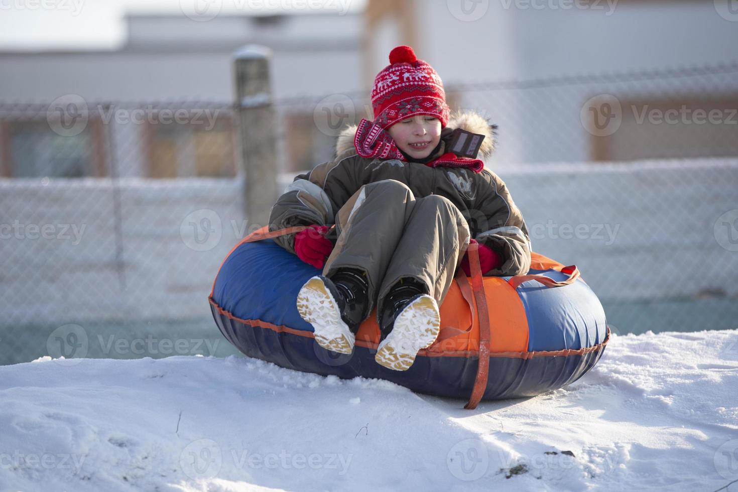 en Lycklig pojke upp i de luft på en rör sledding i de snö.. en pojke diabilder ner en kulle i vinter. foto