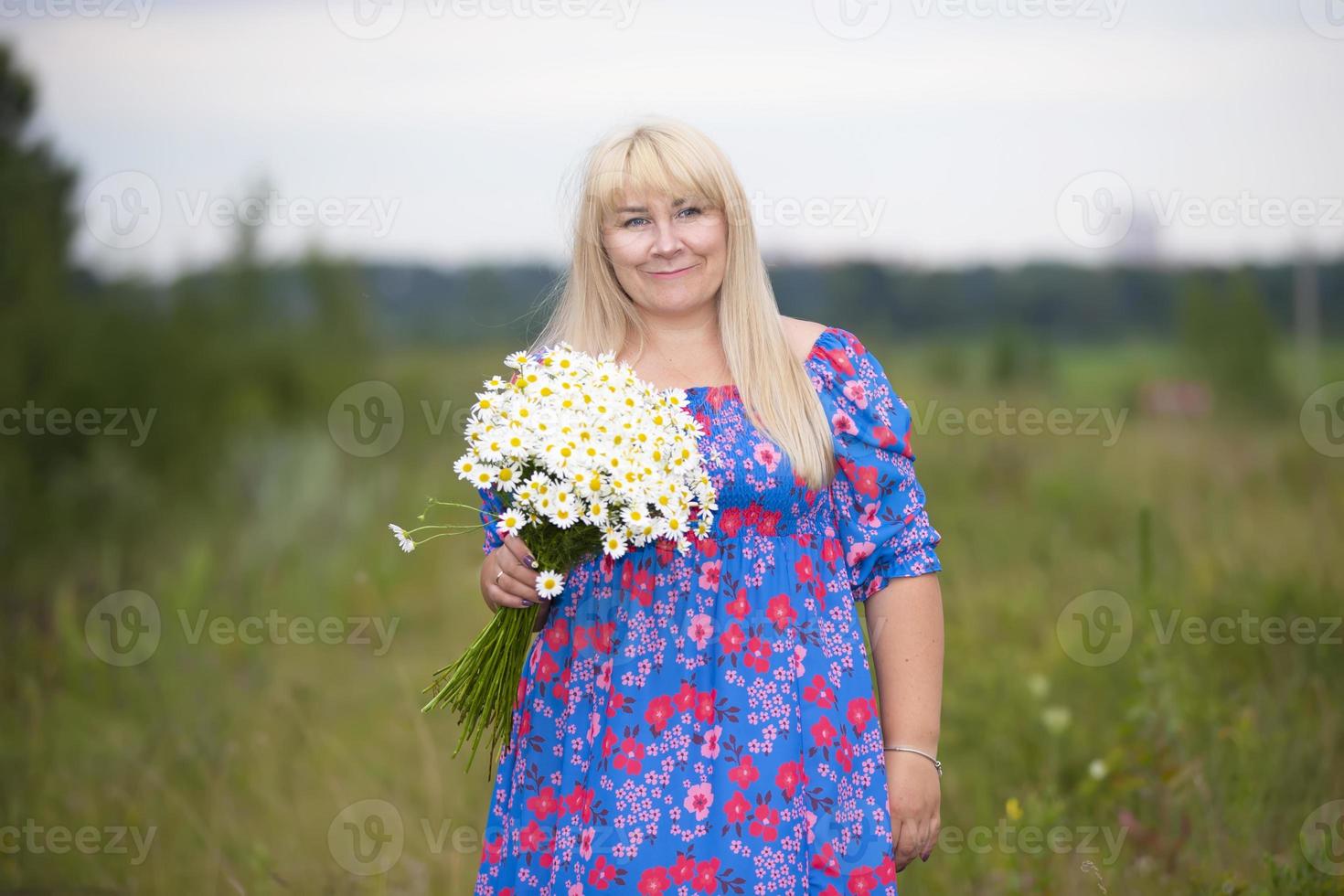 skön plus storlek kvinna med vit hår i en sommar klänning Framställ utomhus med prästkragar. knubbig flicka i en äng med blommor. foto