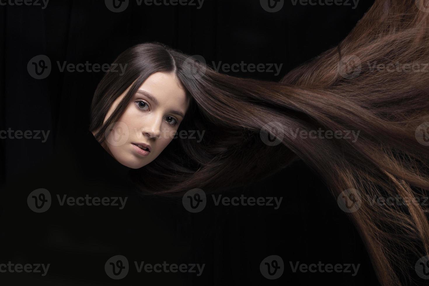 lång mörk hår. de ansikte av en flicka med strömmande hår på en mörk bakgrund. foto