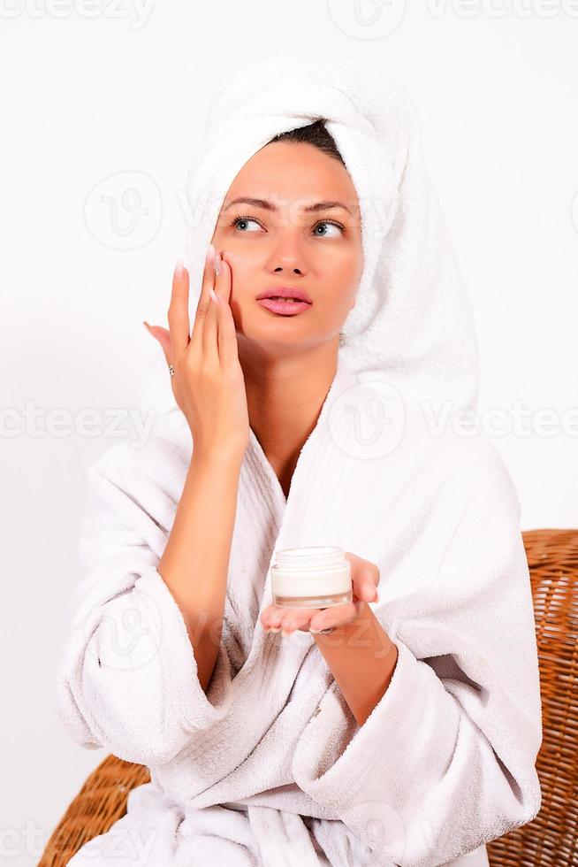 skönhet, vård, hälsa, en flicka i en vit täcka tar vård av själv, hon utstryker någon på henne ansikte foto