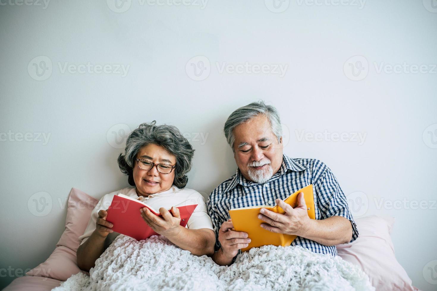 äldre par som ligger på sängen och läser en bok foto