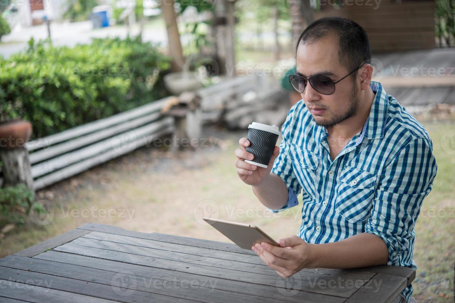 ung man sitter utomhus vid ett träbord och kopplar av med tabletten foto