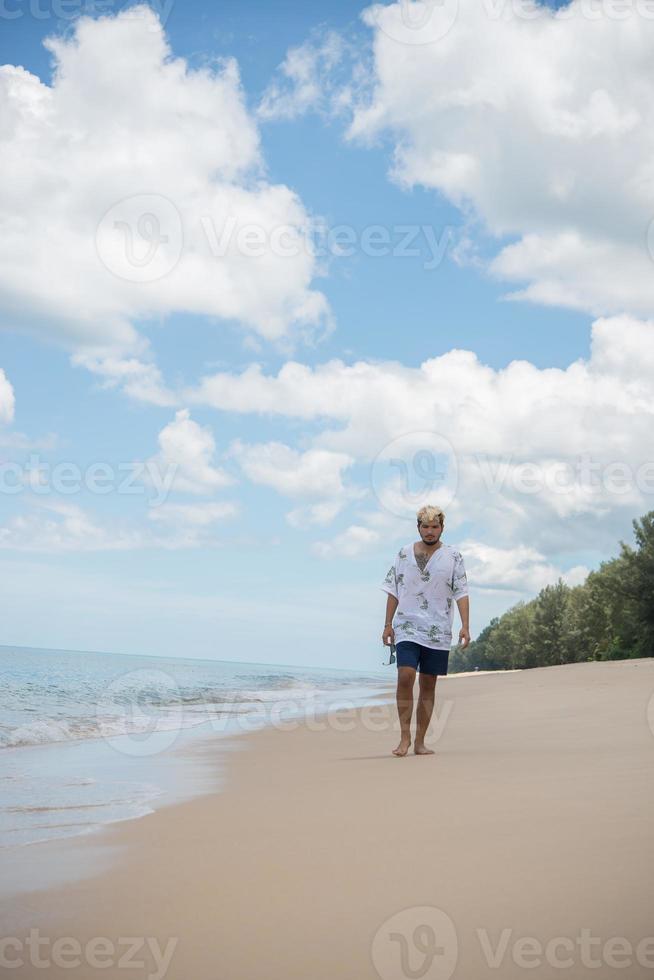 hipster man går på bakgrunden av vackra stranden med vita moln och fin himmel foto