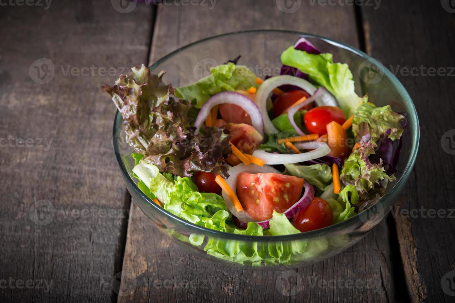 färsk grönsaksallad i glasskål på träbakgrund foto