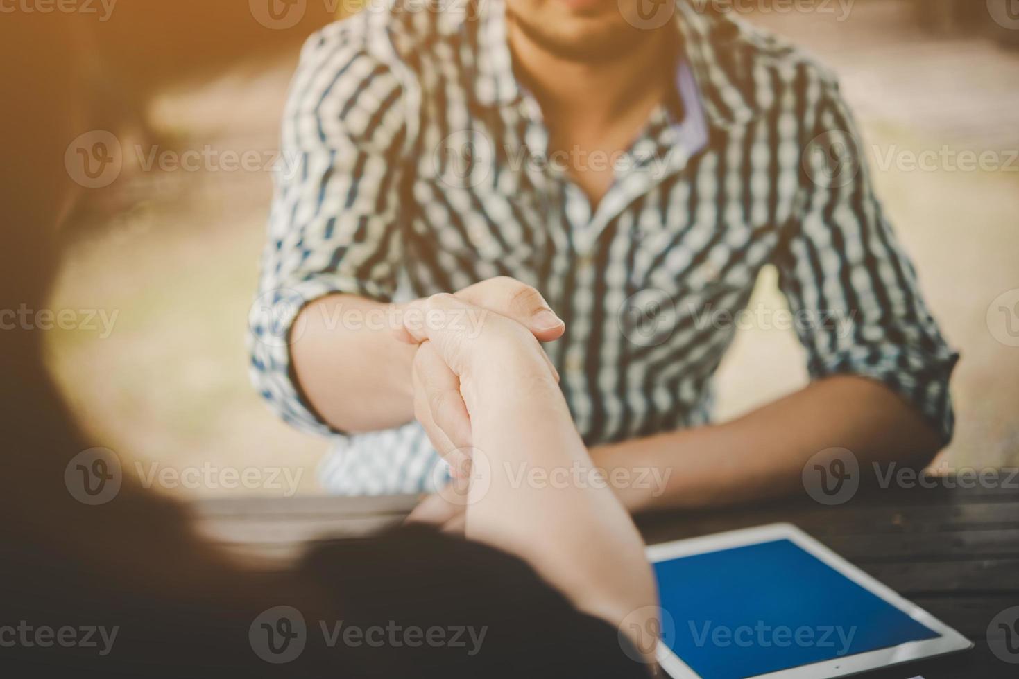 närbild av två affärsmän som skakar hand medan du sitter på arbetsplatsen foto