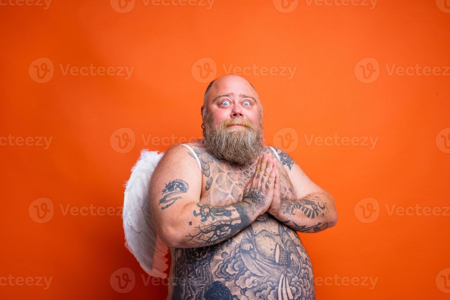 fett rädd man med skägg , tatueringar och vingar handlingar tycka om ett ängel foto