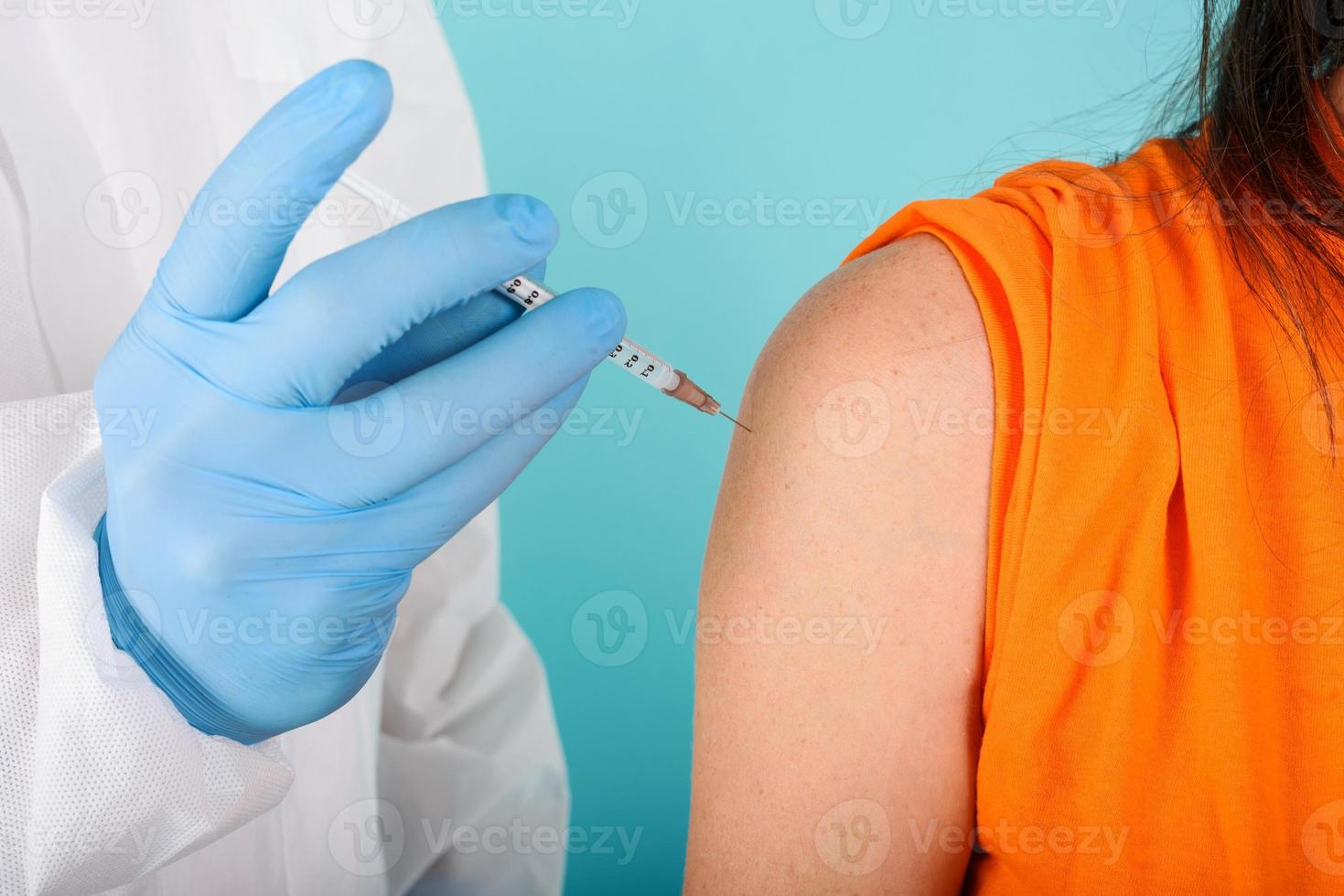 läkare läkare injicerar vaccin med spruta mot covid19 coronavirus. cyan bakgrund foto