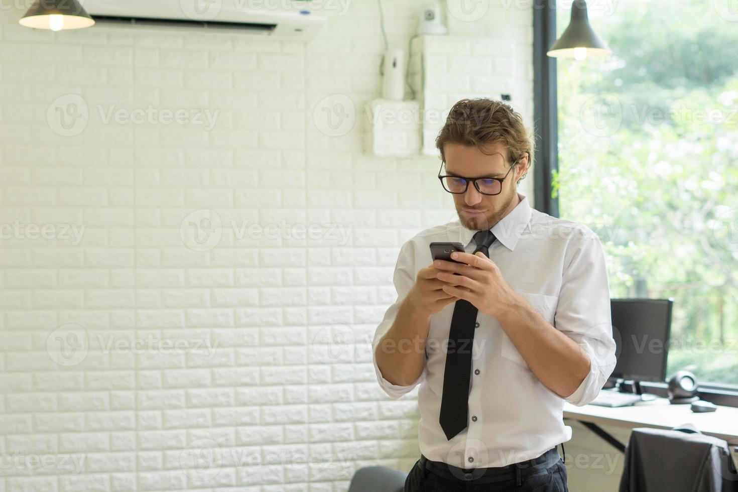 ung affärsman som använder smartphonen medan han arbetar på kontoret foto