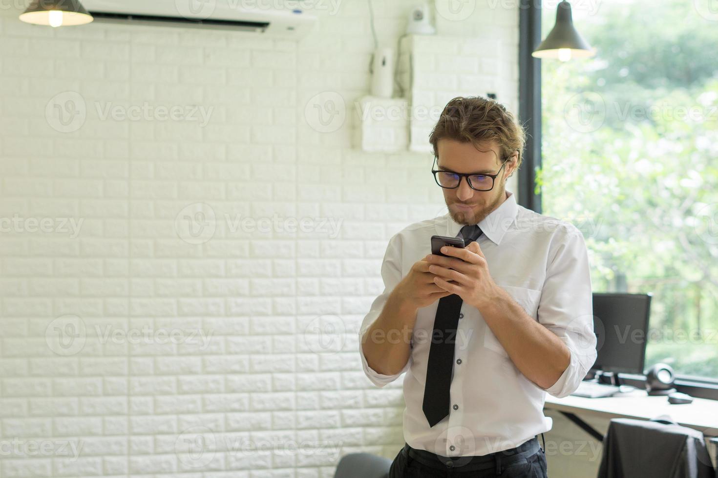 ung affärsman som använder smartphonen medan han arbetar på kontoret foto
