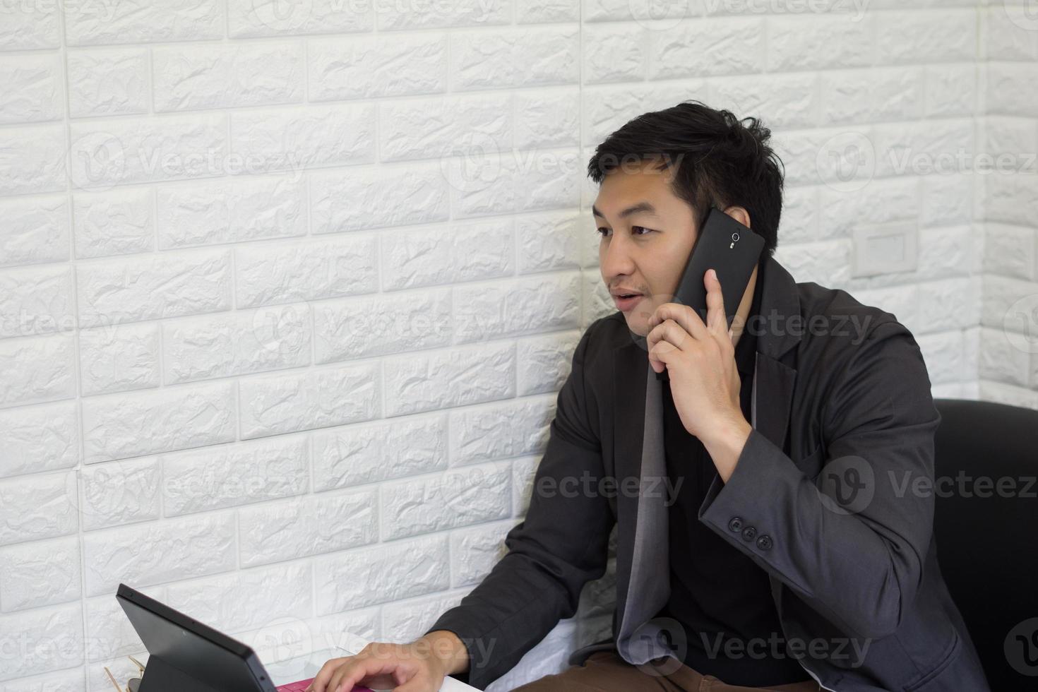 ung affärsman som använder smartphonen medan han arbetar på sin bärbara dator i regeringsställning foto
