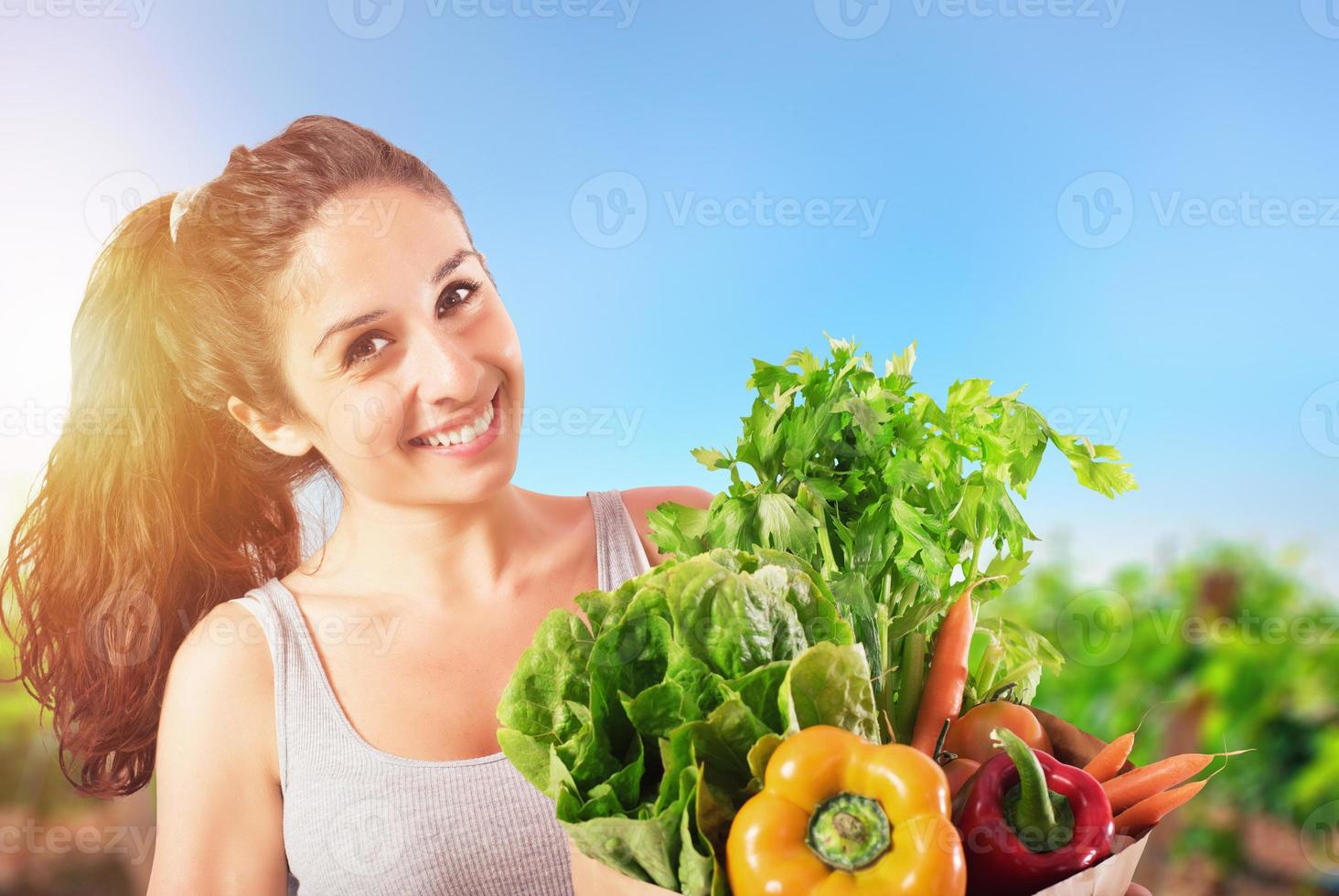 flicka med väska full av nyligen köpt grönsaker med de vegetabiliska trädgård på bakgrund foto