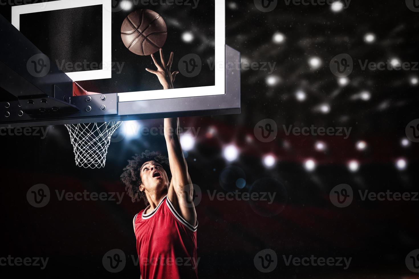 basketboll spelare i röd enhetlig Hoppar hög till göra en slam dunka till de korg foto