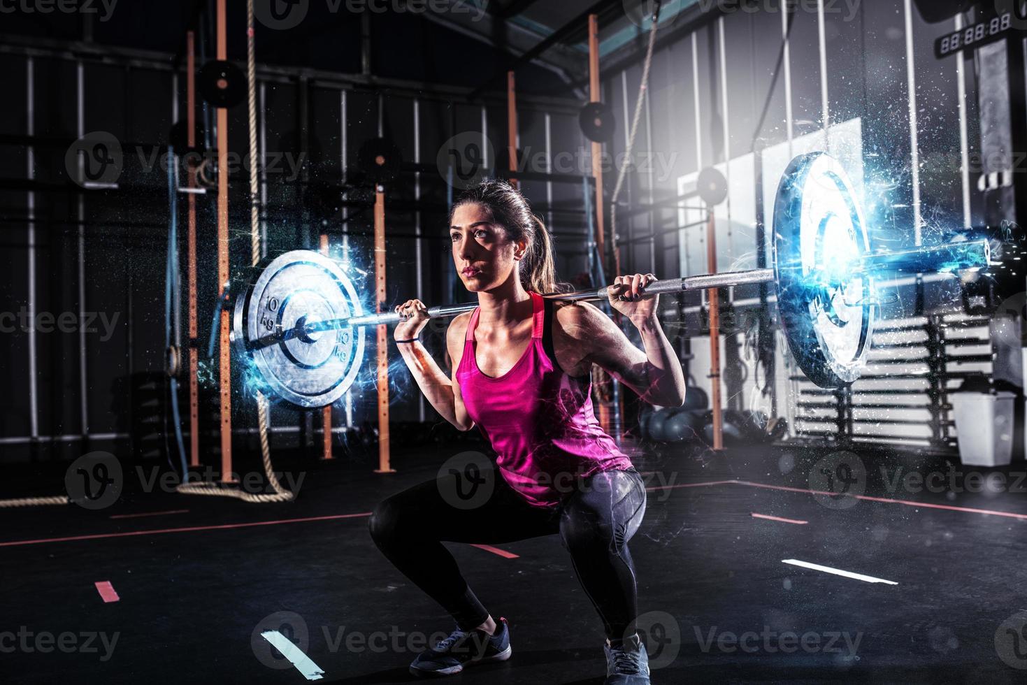 atletisk flicka Arbetar ut på de Gym med en skivstång med blå energi effekter foto