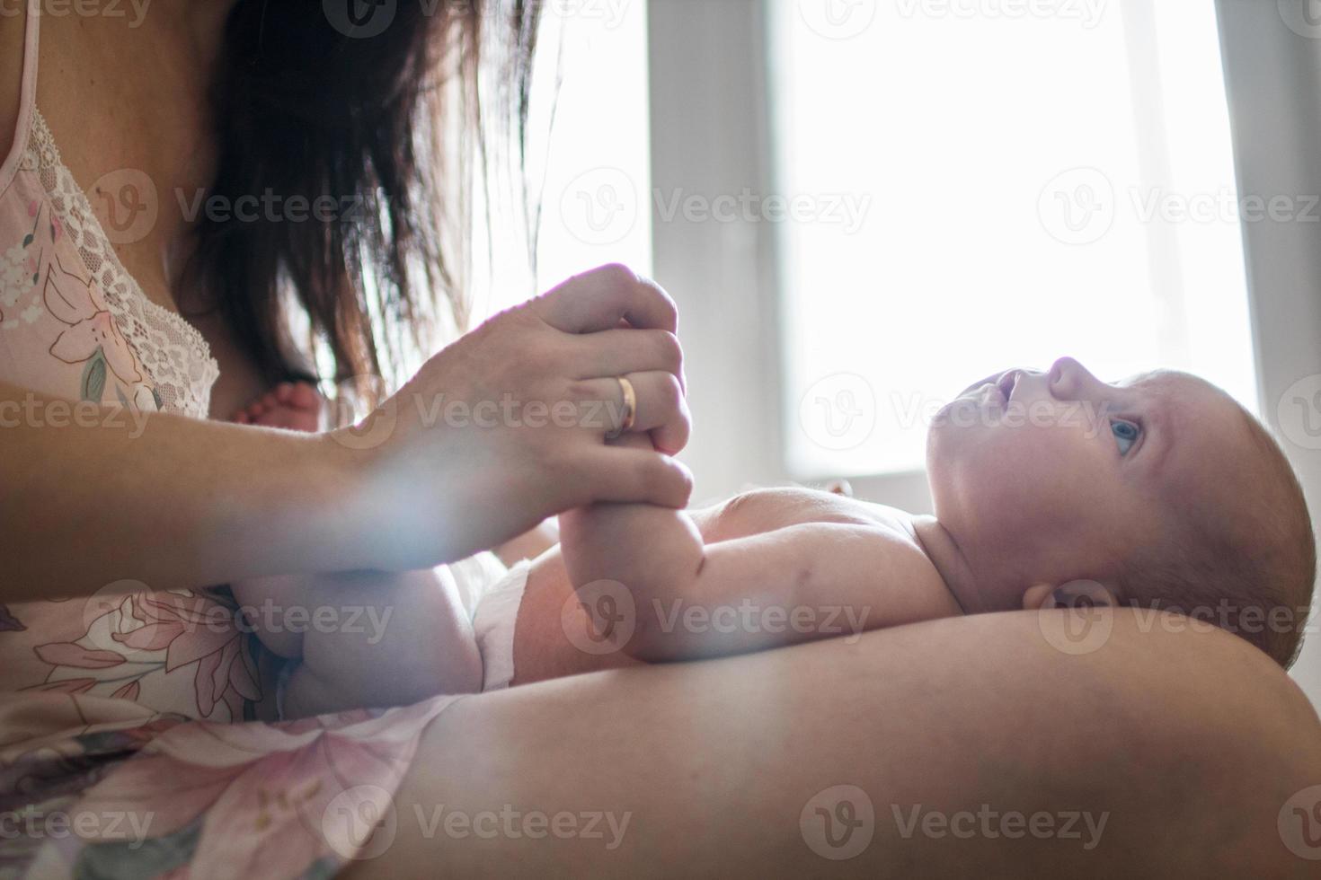 mor med en bebis på en säng förbi de fönster foto