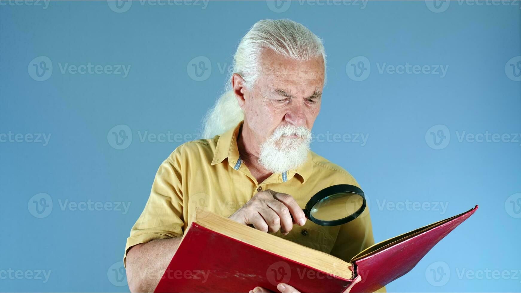 gammal man ser på bok med förstorande glas foto