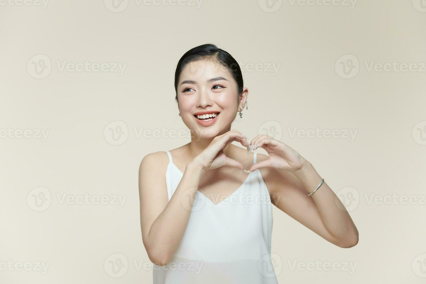 porträtt av positiv ung lady med friska slät hud innehav händer i de form av en hjärta nära ansikte foto