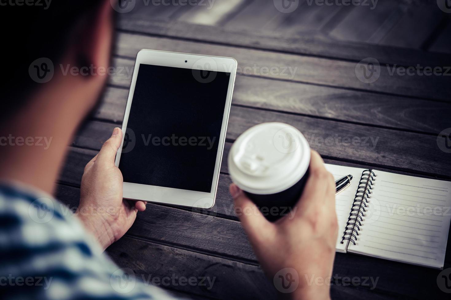 ung man som använder den digitala minnestavlan medan han dricker kaffesammanträde hemma i trädgården foto