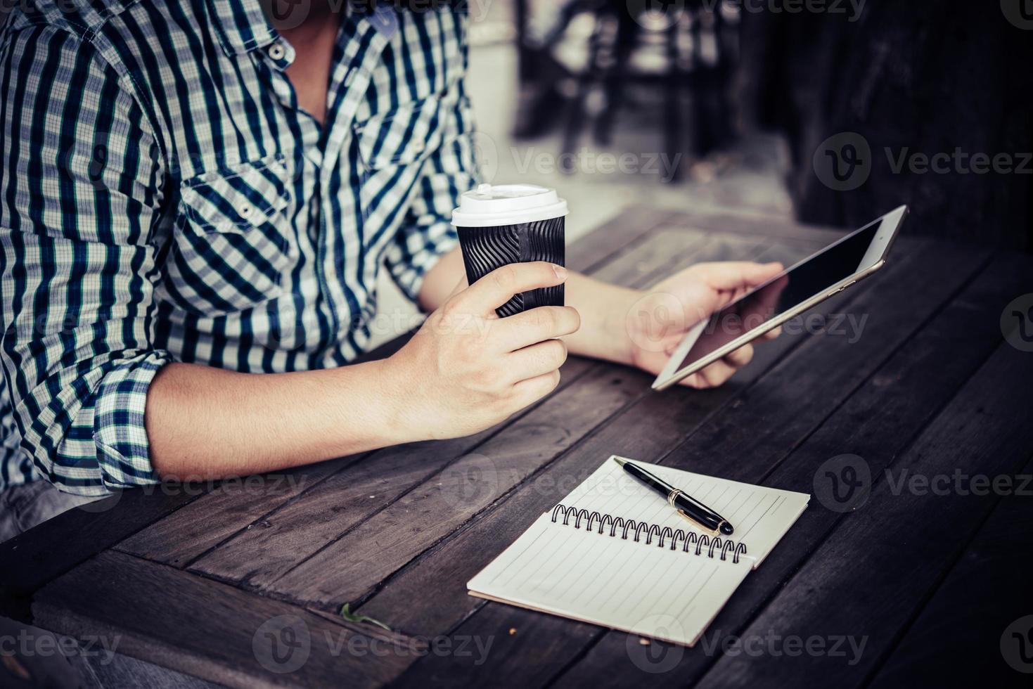 ung man som använder den digitala minnestavlan medan han dricker kaffesammanträde hemma i trädgården foto