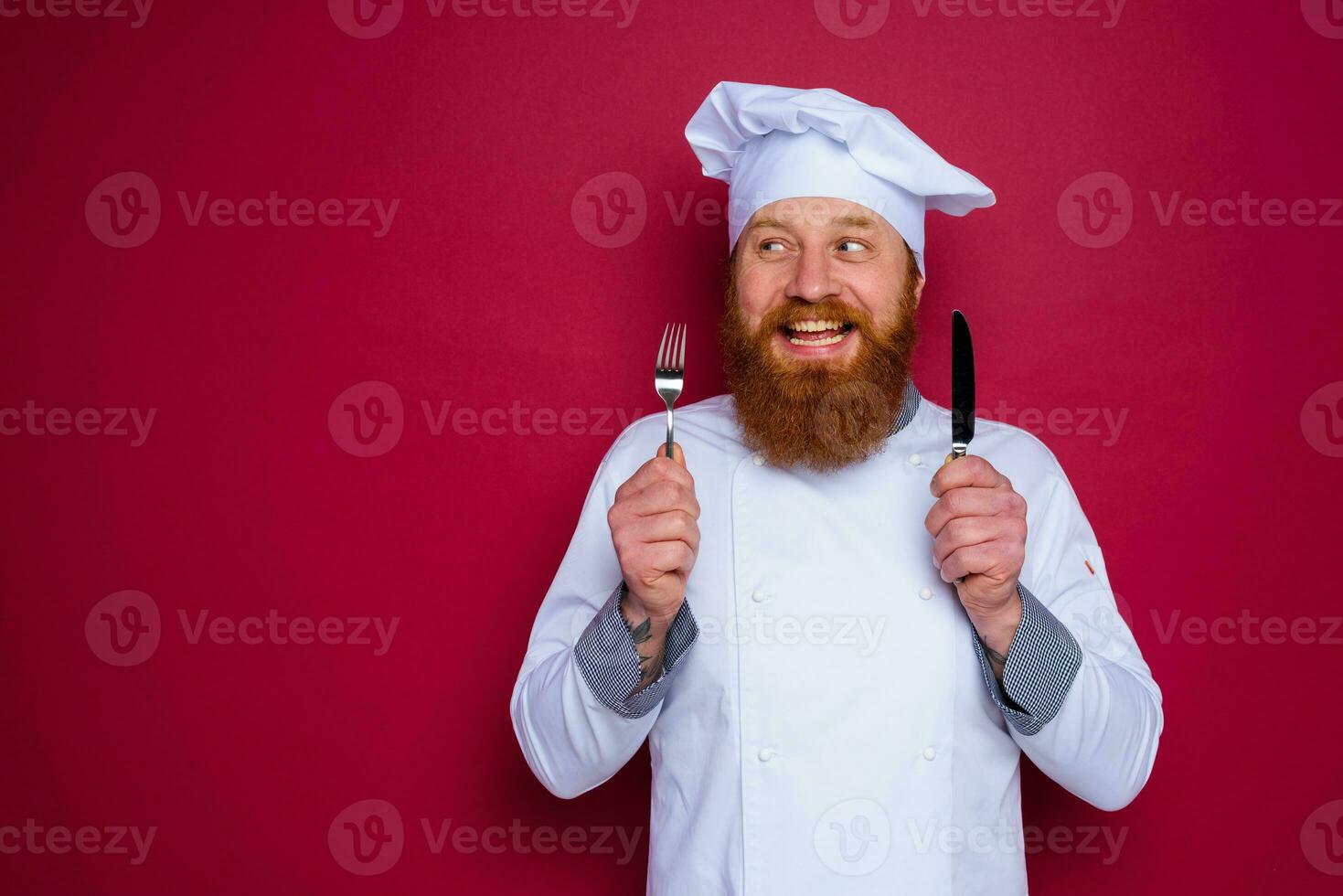 Lycklig kock med skägg och röd förkläde innehar bestick i hand foto