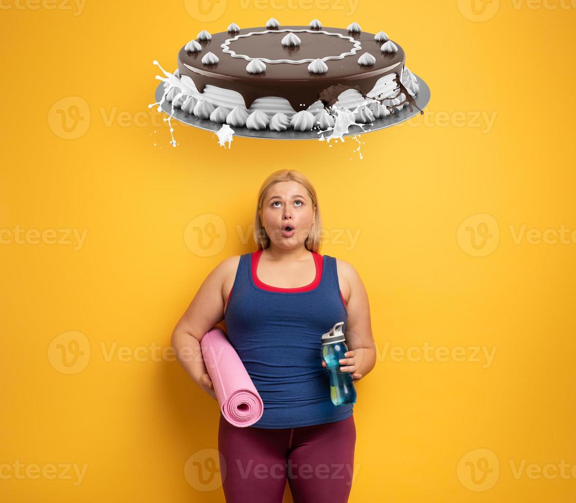 fett flicka tänker till äta sötsaker istället av do Gym. gul bakgrund foto
