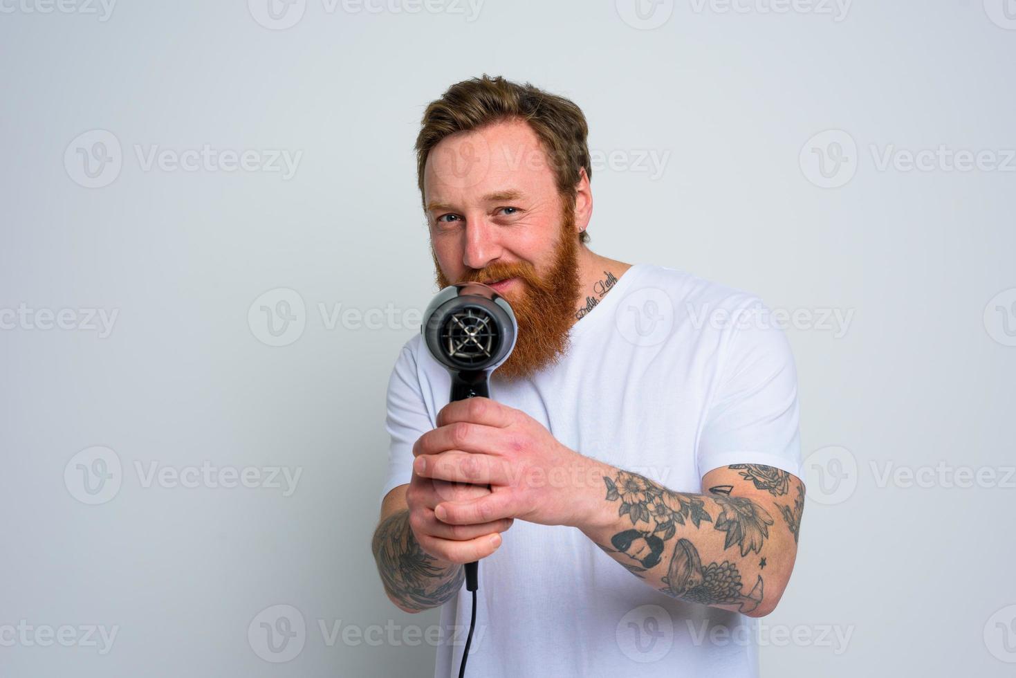 Lycklig man med skägg spela med hår torktumlare en handeldvapen foto