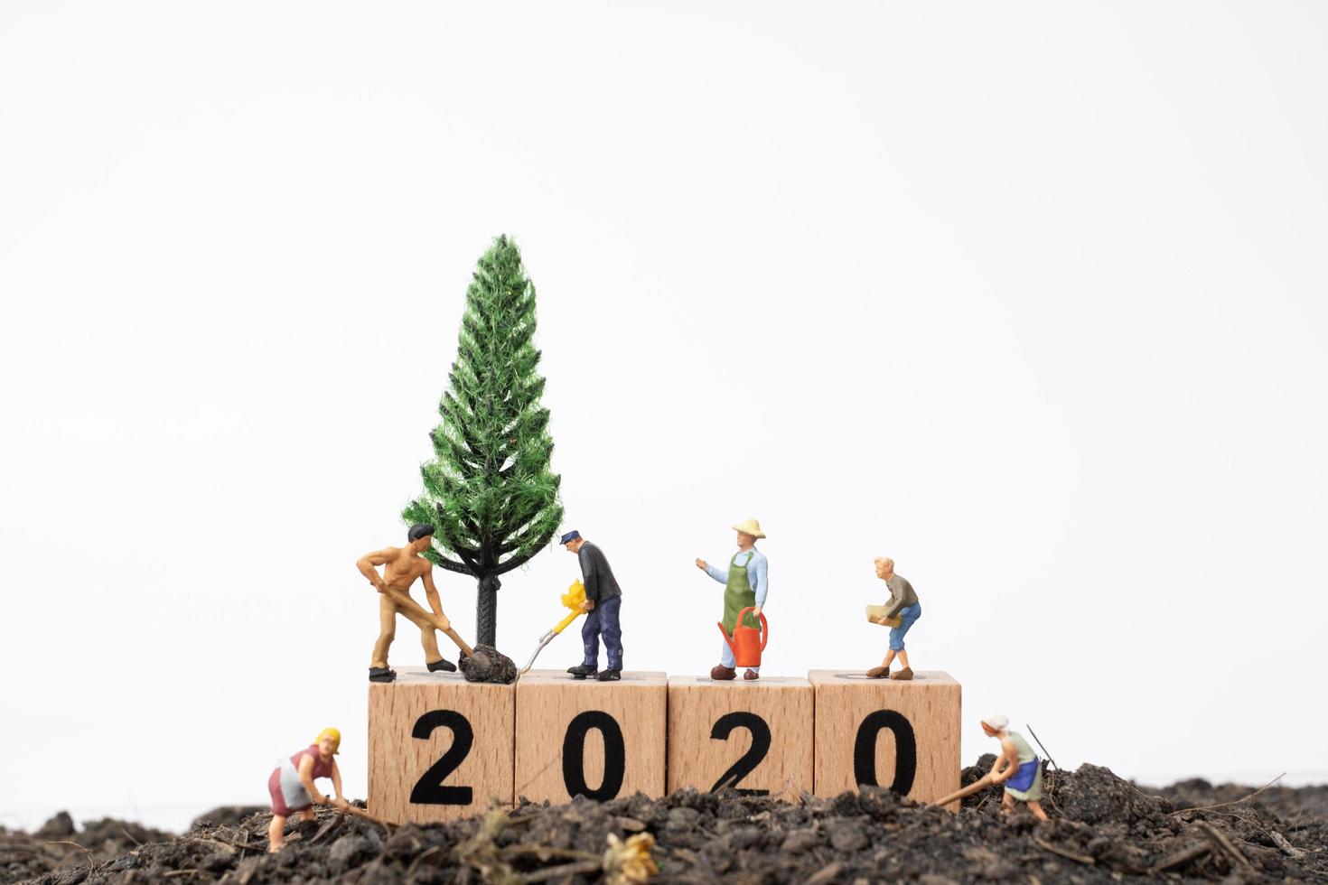 miniatyrträdgårdsmästare som tar hand om ett träd på ett träblock med nummer 2020, koncept för gott nytt år foto