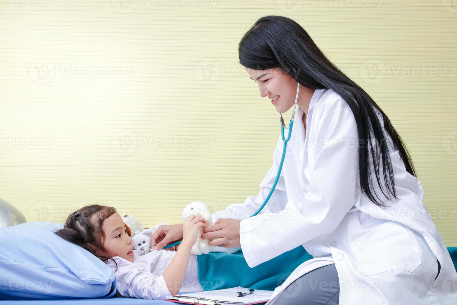 asiatisk kvinna doktorer använda sig av stetoskop till kolla upp de hjärtslag en liten flicka i en sjukhus säng. begrepp av barn vård. foto