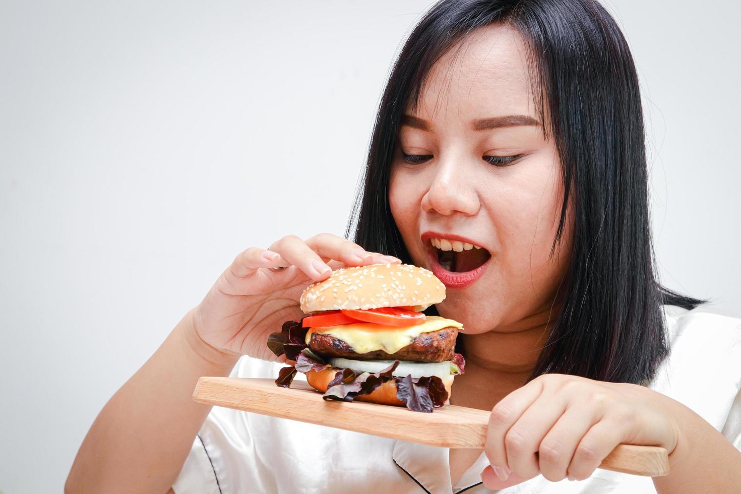 fett asiatisk kvinnor äta stor hamburgare, vit bakgrund. hälsa begrepp. människor vem är övervikt. foto