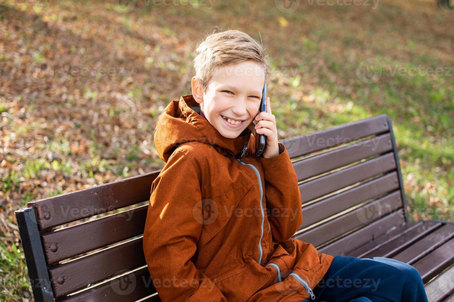 de pojke är talande på de telefon Sammanträde på en bänk och skrattande foto