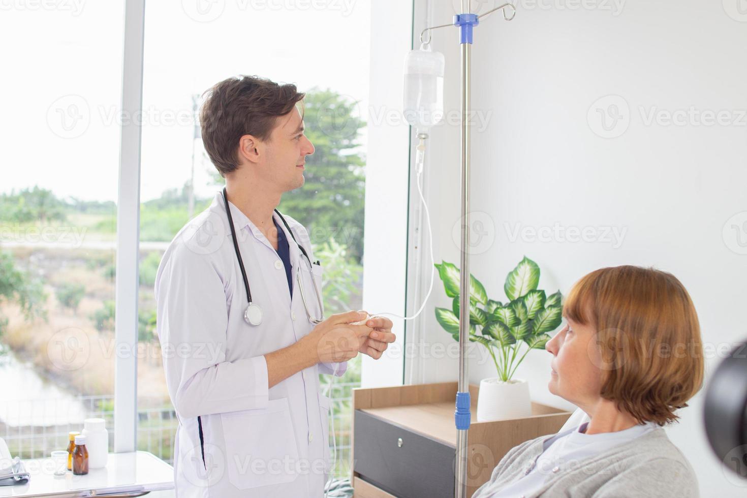 de läkare är granskning de patient i de sjukhus. caucasian läkare bär klänning och stetoskop ser på vanligt salin med en kvinna patient på de sjukhus. foto