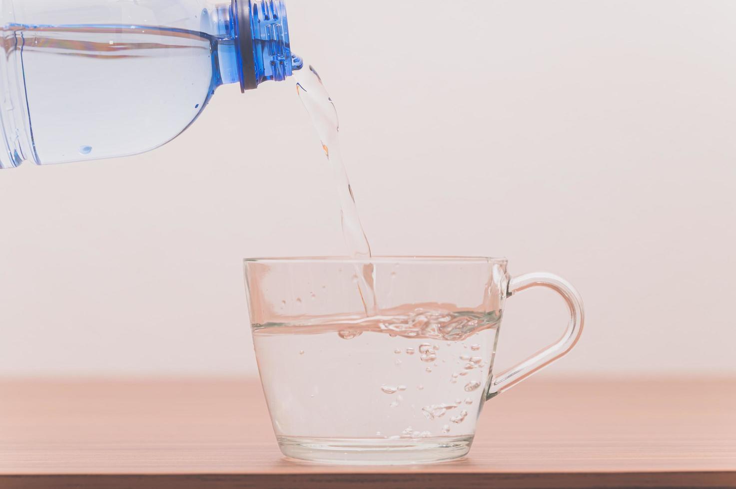 flaska dricksvatten som häller i glas foto