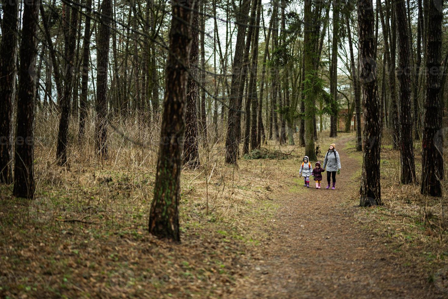 mor och två döttrar med ryggsäckar gående längs de skog väg tillsammans. foto