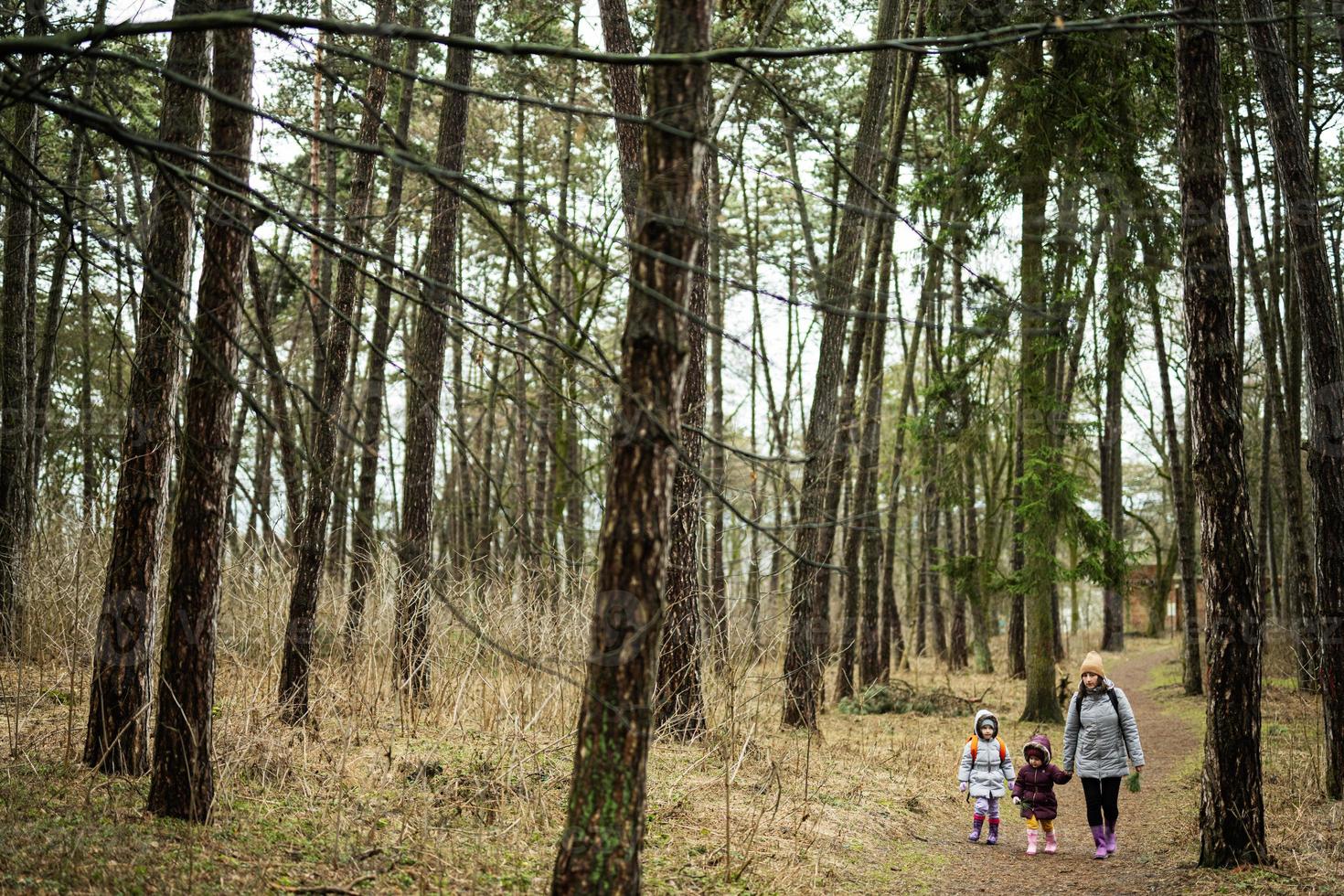 mor och två döttrar med ryggsäckar gående längs de skog väg tillsammans. foto