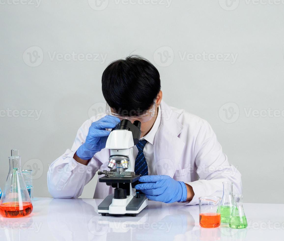 asiatisk manlig studerande forskare i reagens blandning laboratorium i en vetenskap forskning laboratorium med testa rör av olika storlekar och mikroskop. på de tabell i laboratorium kemi labb vit bakgrund. foto