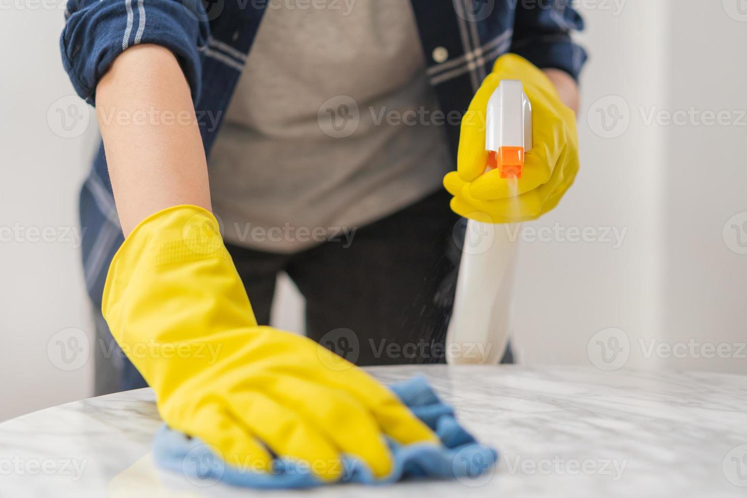 rengöring hygien, stänga upp hand av hembiträde, servitris kvinna bär gul skyddande handskar medan rengöring på trä tabell, använda sig av blå trasa avtorkning till damm och spray i restaurang. hushållning städning, renare foto