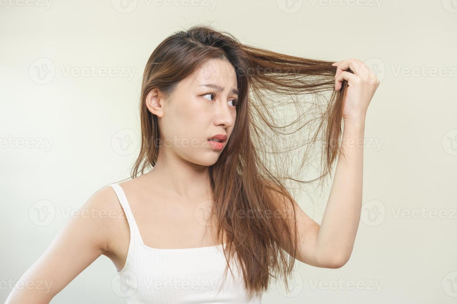 skadad hår, frustrerad asiatisk ung kvinna, flicka hand i innehav delning slutar, rörig oborstad torr hår med ansikte chock, lång rufsig hår, hälsa vård av skönhet. porträtt isolerat på bakgrund. foto