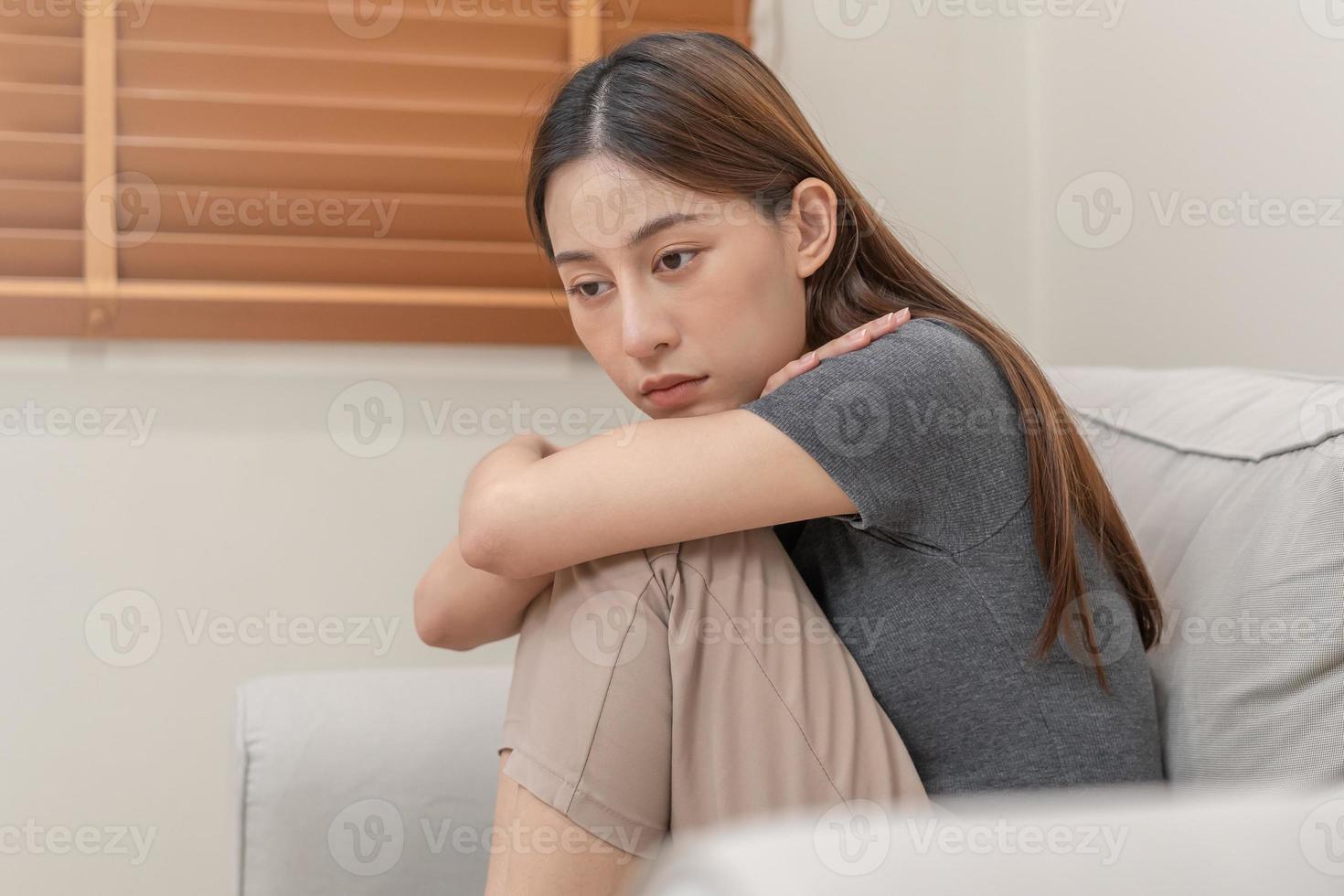 mental hälsa, deprimerad ledsen asiatisk ung kvinna, flicka Sammanträde på soffa, soffa, uttryck till ansikte svårighet, fel och utmattad. omtänksam orolig lidande depression känsla ensam, ensam på Hem foto