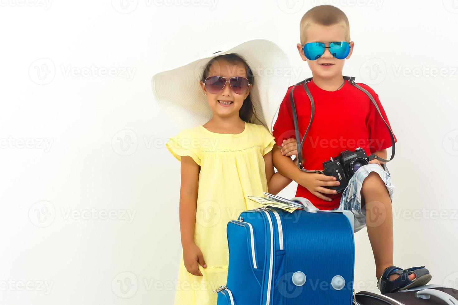 barn resa - pojke med en kamera, flicka i solglasögon och vit hatt stå nära en resväska foto