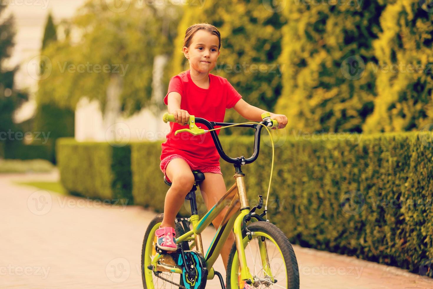 barn ridning cykel. unge på cykel i solig parkera. liten flicka njuter cykel rida henne sätt till skola värma sommar dag. preschooler inlärning till balans cykel sport för ungar. foto