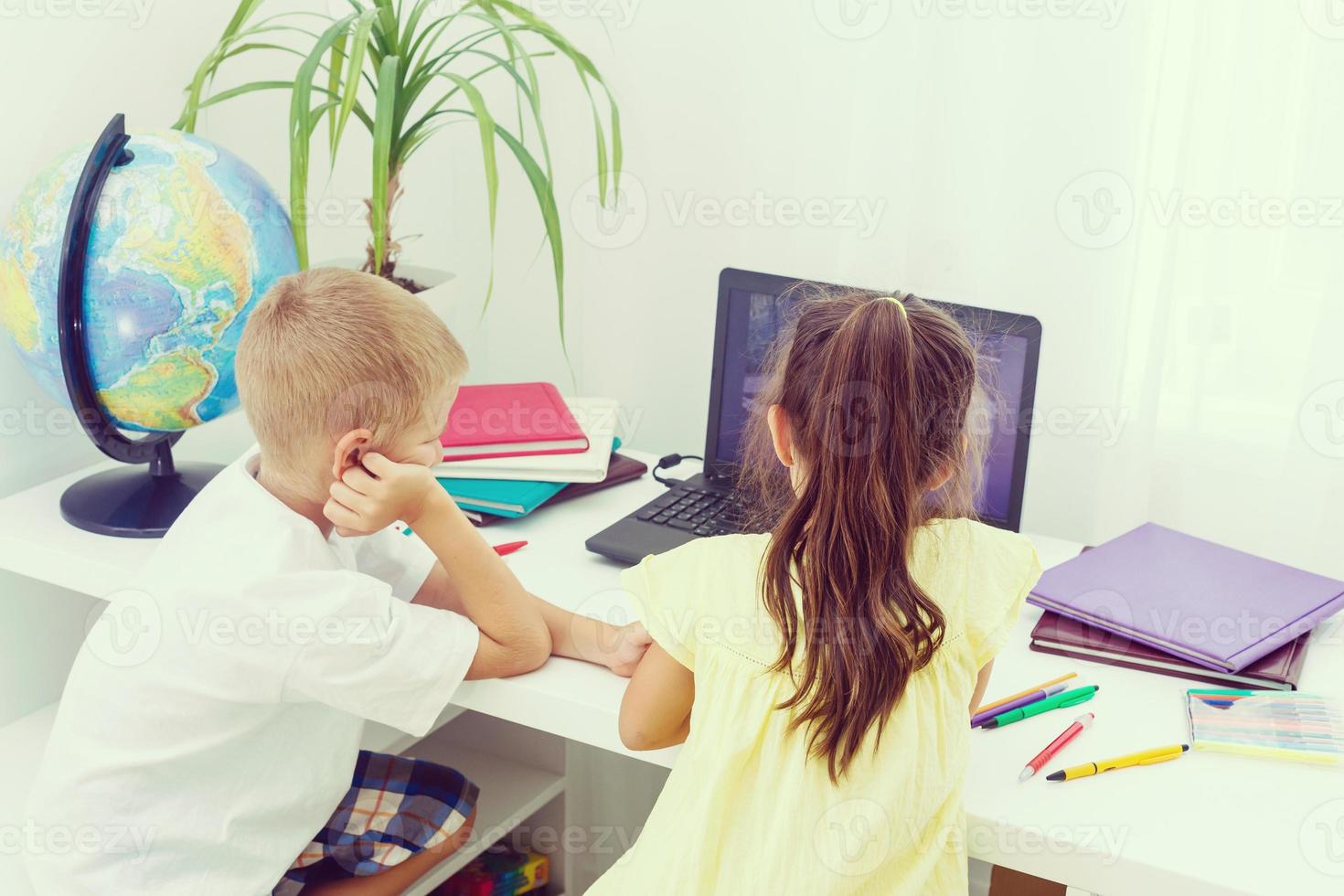 söt liten barn studerar på studie tabell med lugg av böcker, pedagogisk klot, isolerat över ljus blå Färg foto