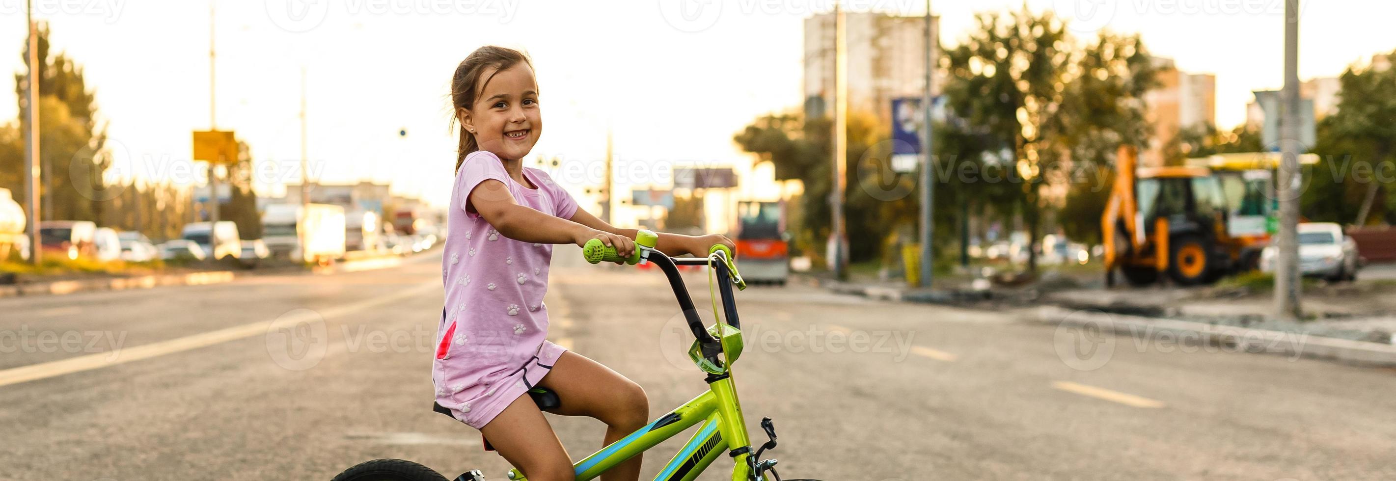 barn inlärning till kör en cykel på en uppfart utanför. liten flickor ridning Cyklar på asfalt väg i de stad bär hjälmar som skyddande redskap. foto