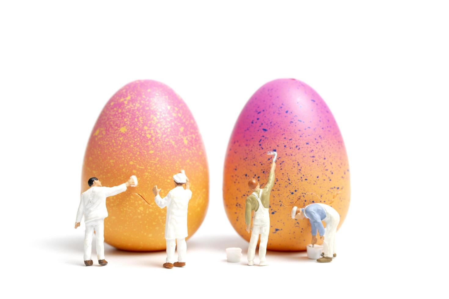 miniatyrfolk som målar påskägg för påskdag på en vit bakgrund foto