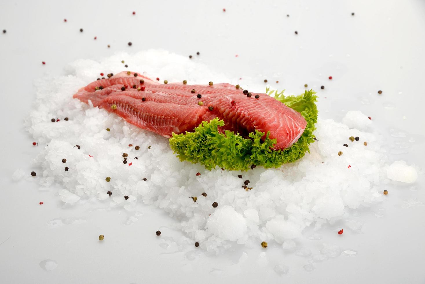 färsk rå fiskfilébiff på is med peppar och sallad på vit bakgrund foto
