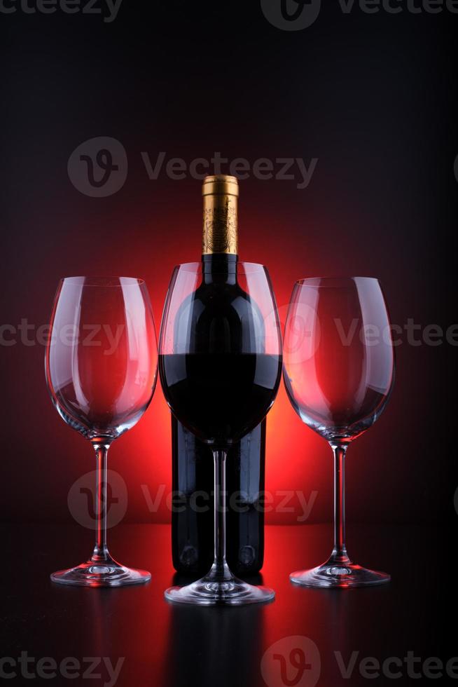 vinflaskor och fullt glas med röd och svart bakgrund foto